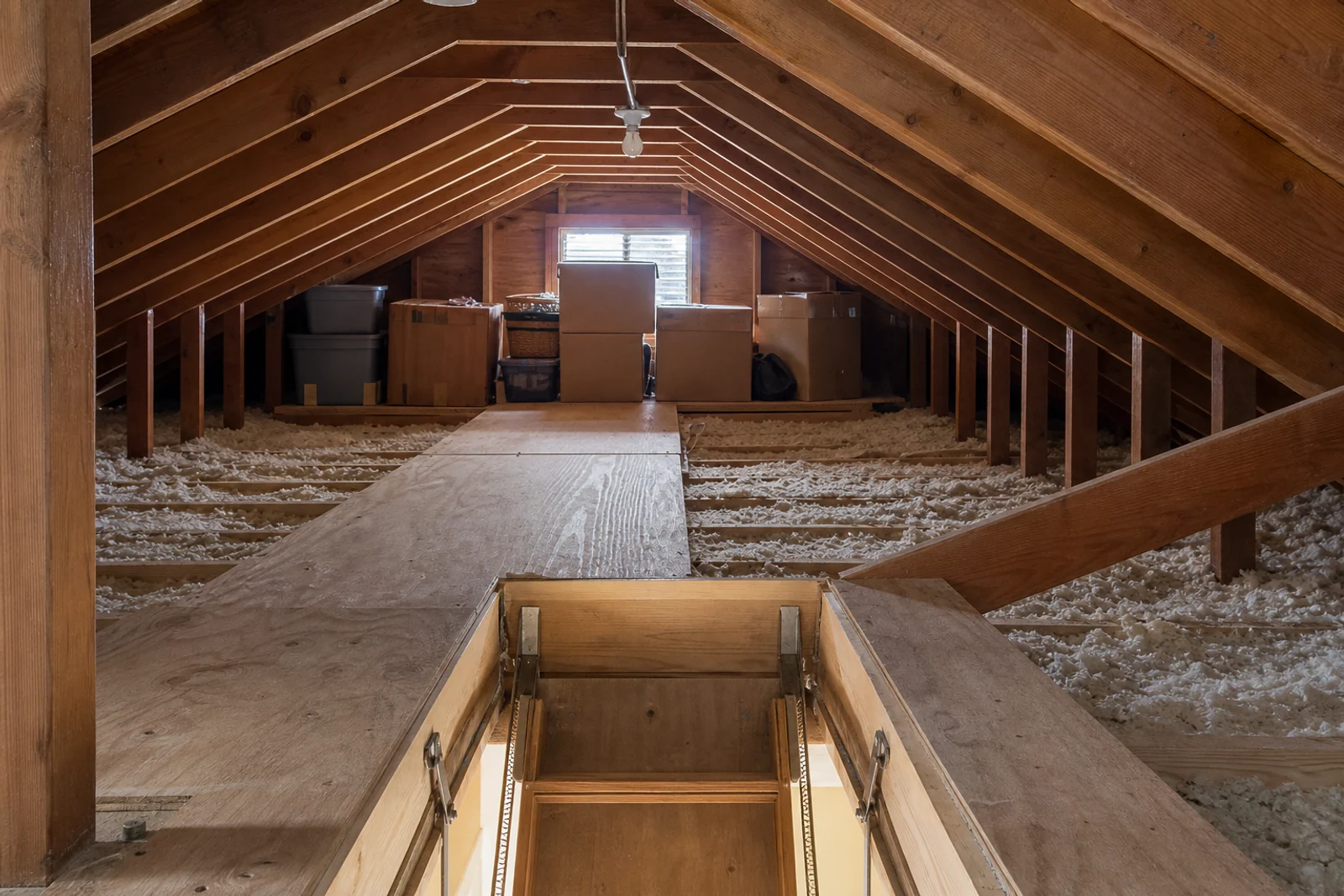 Residential attic with a walking surface, stored boxes, low rafters, and an open access hatch