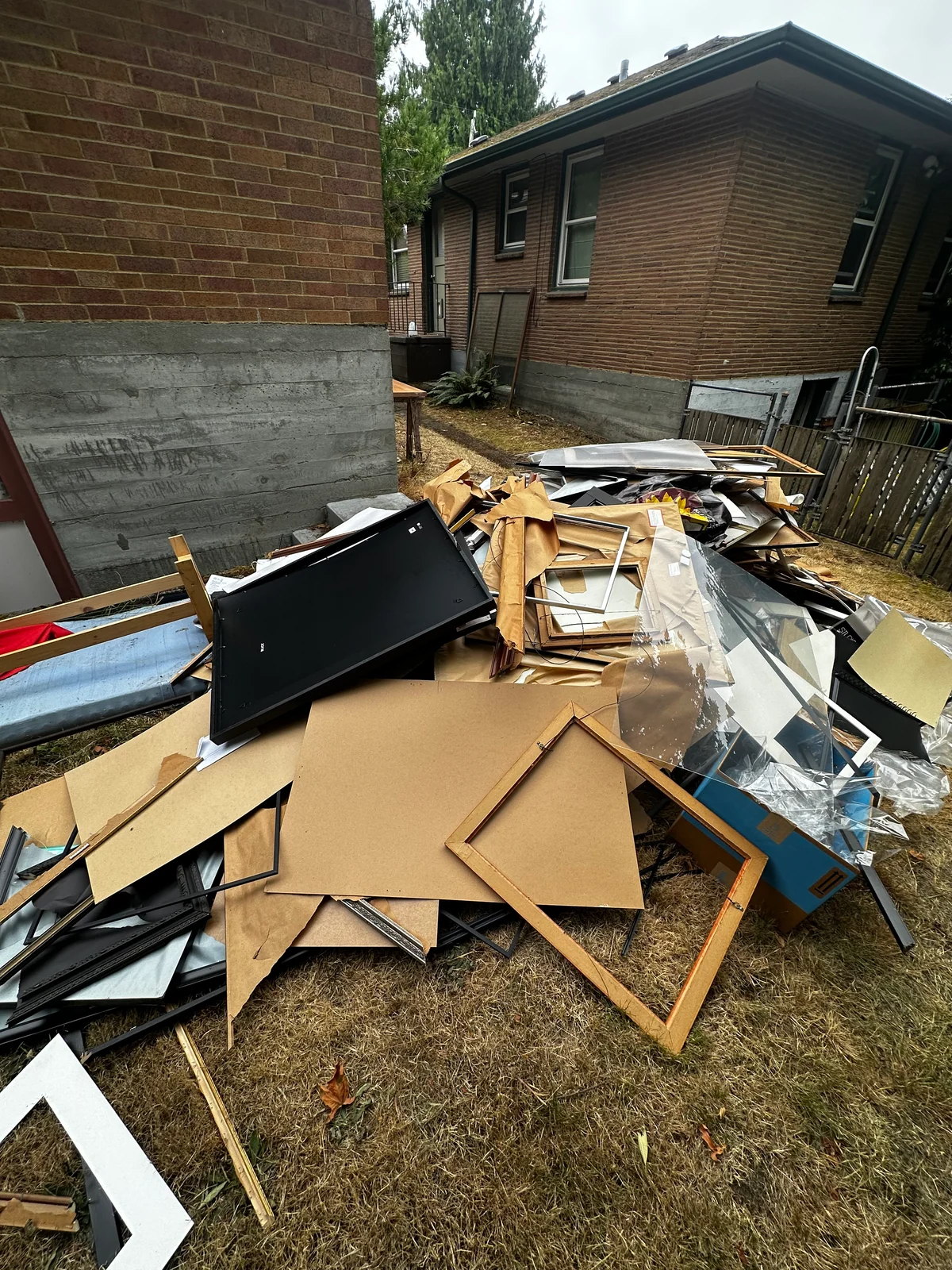 Second view of frames and cardboard piled across the grass beside the building